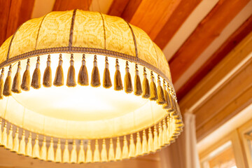 Large yellow fabric lampshade with fringe as an element of vintage decor. Old style retro lamp...