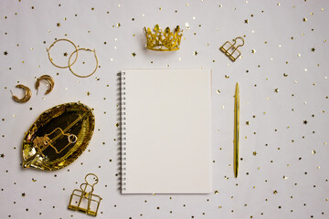 Golden crown with notebook, pen and golden leave over the glitter background. 