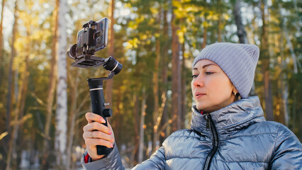 Woman Holding On Handheld Film 3-axis Gimbal Stabilization Device in Winter for Smartphone. Girl...