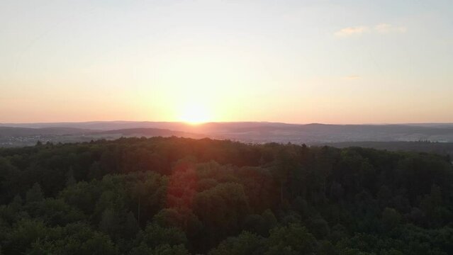 fast-flying footage over a huge forest at an orange sunset and giving beautiful solar flares in the images with mountains in the background