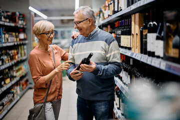 Happy senior couple choosing wine while shopping in supermarket.