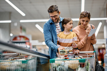 Happy parents with daughter going through checklist while buying in supermarket.