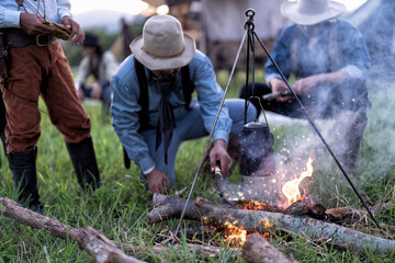 Cowboy groups stopped camping and rest and brewed coffee on 3 legs steel support hanging kettle coffee pot, use knife to cut wooden piece and fire with smoke and fire spark dust flow in the air 

