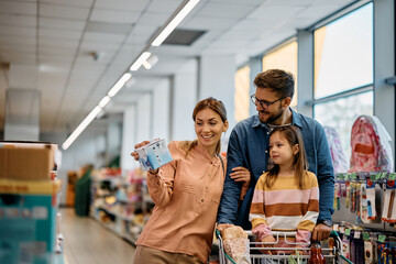 Happy parents with their small daughter buying in supermarket.