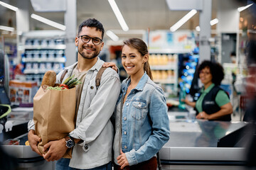 Young happy couple shopping at supermarket and looking at camera.