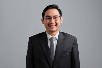Portrait of smiling handsome young businessman in formal suit standing and looking at camera with positive expression isolated on grey background