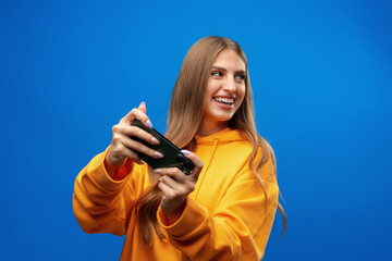 Excited young woman playing mobile video game on smartphone against blue background