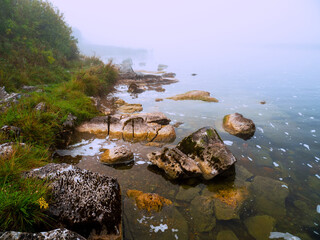 Warm orange color rocks in a river or lake and cool fog in the background. Calm water surface. Beautiful nature scene. Nobody, selective focus. Warm and cool tone.