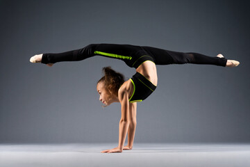 Flexible little girl doing acrobatic stunts while standing on her hands. The gymnast is dressed in...