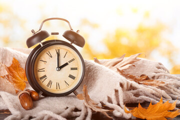 Alarm clock, acorns, scarf and autumn leaves on table outdoors. Daylight saving time end - obrazy, fototapety, plakaty