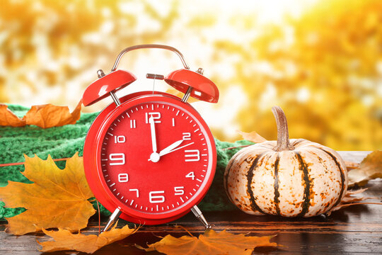 Alarm clock, pumpkin, sweater and autumn leaves on table outdoors