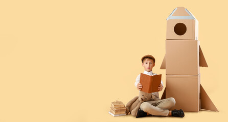 Surprised little boy with books, toy and cardboard rocket on beige background with space for text