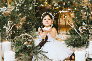 little beautiful asian girl in white dress and crown sit in loft room decorated with wooden...