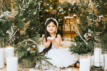 little beautiful asian girl in white dress and crown sit in loft room decorated with wooden greenhouse and Christmas trees with twinkle lights, diverse people, Christmas and New Year celebration