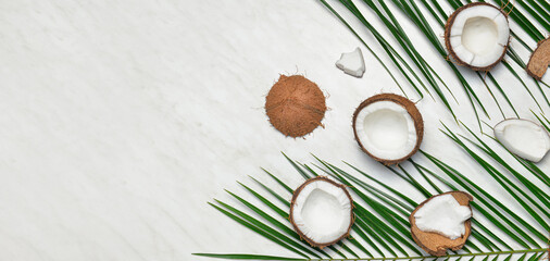 Obraz na płótnie Canvas Ripe cut coconuts and palm leaves on light background with space for text, top view