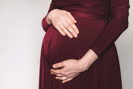 Pregnancy, maternity, preparation, baby expectation concept. 40 weeks of pregnancy. Pregnant woman in bordo dress touching belly, preparing go to maternity hospital for childbirth. White background