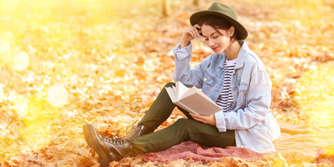 Pretty young woman reading interesting book in autumn park