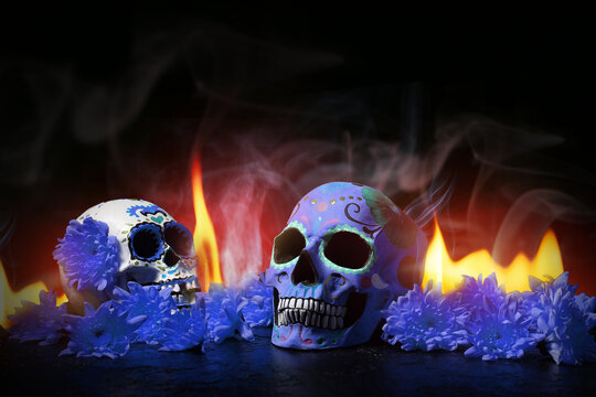 Painted human skulls for Mexico's Day of the Dead (El Dia de Muertos), flame and flowers on dark background