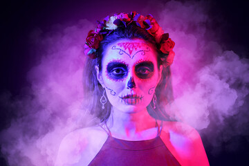 Young woman with painted skull on her face against dark background. Celebration of Mexico's Day of...