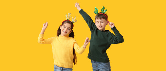 Funny dancing little children with reindeer horns on yellow background