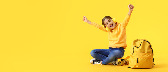 Happy little schoolgirl listening to music on yellow background with space for text