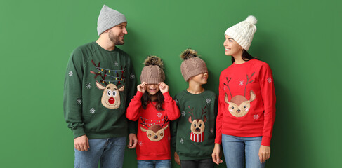 Happy family in funny Christmas sweaters on green background