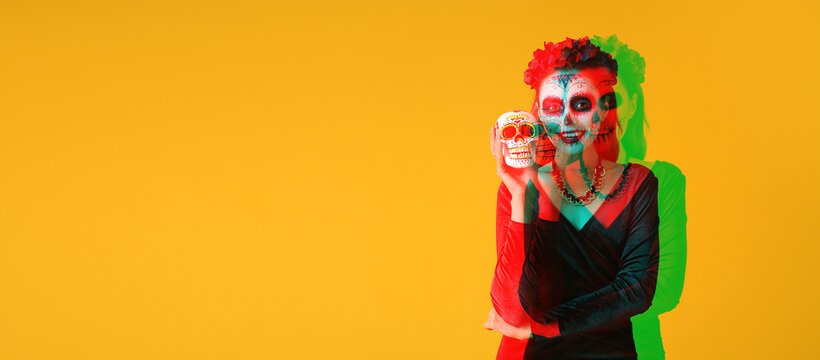 Young woman with painted skull on her face for Mexico's Day of the Dead (El Dia de Muertos) against yellow background with space for text