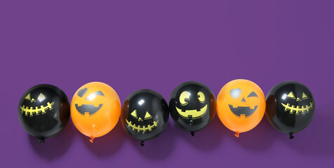 Row of funny Halloween balloons on purple background with space for text