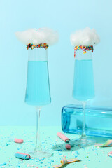Glasses with tasty cotton candy cocktail and sweets on color background