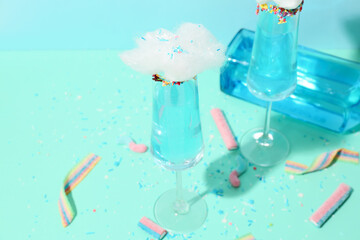 Glasses with tasty cotton candy cocktail and sweets on color background