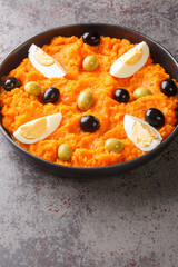 Omek Houria is a Tunisian salad, made with carrots, harissa, garlic, vinegar, olive oil served with egg and olives closeup in the plate on the table. Vertical