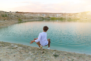 A boy of 8-9 years old throws stones into the water from the shore, fun in nature.