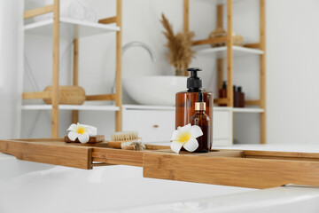 Fototapeta na wymiar Bathtub tray with bath accessories and plumeria flowers, closeup