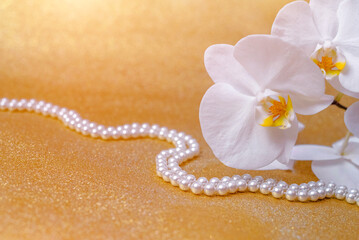 white Orchid and pearl necklace on a shiny gold background
