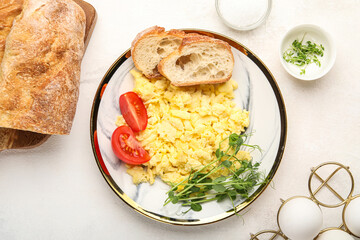 Plate of tasty scrambled eggs, tomatoes, bread and green sprouts on light background