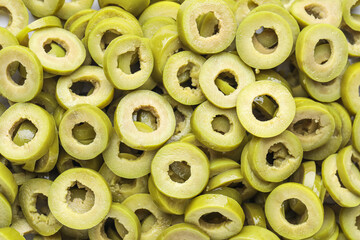 Slices of cut green olives as background, closeup