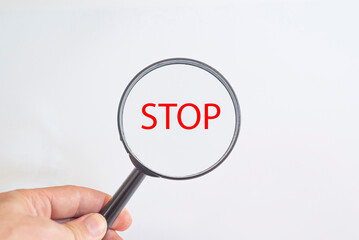 Stop text in magnifying glass.
hand holding a magnifying glass.
Detective and Search risk Idea Concept.