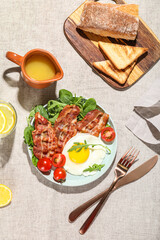Plate with tasty fried egg, bacon, jug of juice and toasts on fabric background