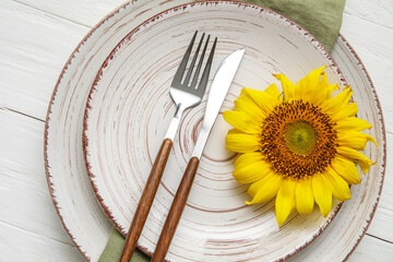 Simple table setting with cutlery and sunflower on white wooden background, closeup