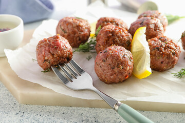 Board with meat balls, dill, lemon slice, baking paper and fork on grunge background, closeup