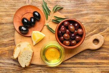 Board with delicious olives, oil and bread on wooden background