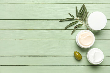 Jars of cream with olive and plant branch on green wooden background