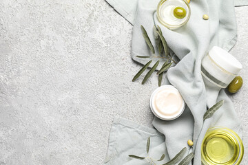 Jars of cream with green olives, oil, plant branches and towel on grunge background