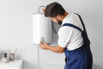 Male plumber adjusting boiler in bathroom - obrazy, fototapety, plakaty