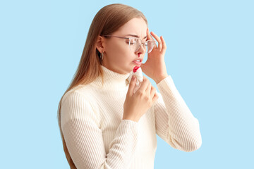 Young woman with nosebleed and tissue on blue background