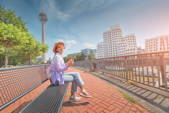 A girl traveler with smartphone enjoys a beautiful view in the Media Bay harbor and TV Tower during a tourist trip or a student education in Dusseldorf, Germany