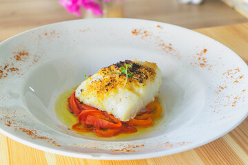 Delicious baked cod with roasted red pepper on wooden table.