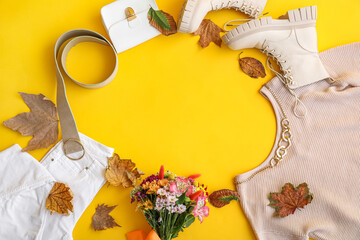 Frame made of stylish clothes, boots, accessories, flowers and autumn leaves on yellow background