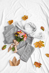 Bouquet of flowers with autumn clothes, accessories and fallen leaves on white fabric background