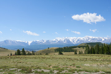 Snow-covered mountain tops against a backdrop of pasture with a beautiful sky. 